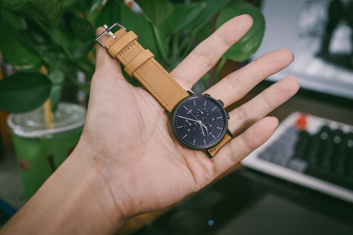 A brown leather watch strap laid beside a wristwatch on a desk